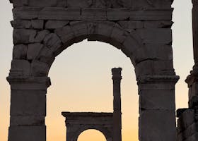 Silhouetted Roman arches against a vibrant sunset sky, historic ruins landscape.